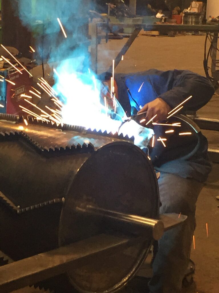 A man welding a large piece of used equipment with sparks and bright lights.